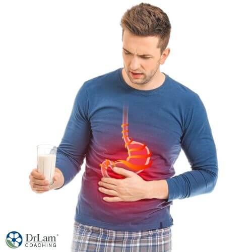 An image of a man holding a glass of milk while holding his stomach
